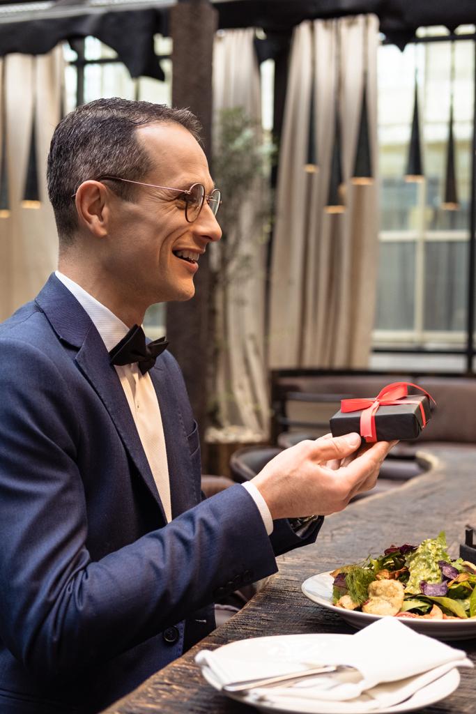 pohledný muž v stylovém obleku prezentaci Valentýn dárek v restauraci - Fotografie, Obrázek