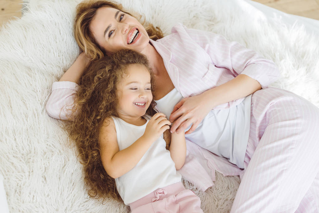 laughing mother and daughter lying on sheep skin blanket - Photo, Image