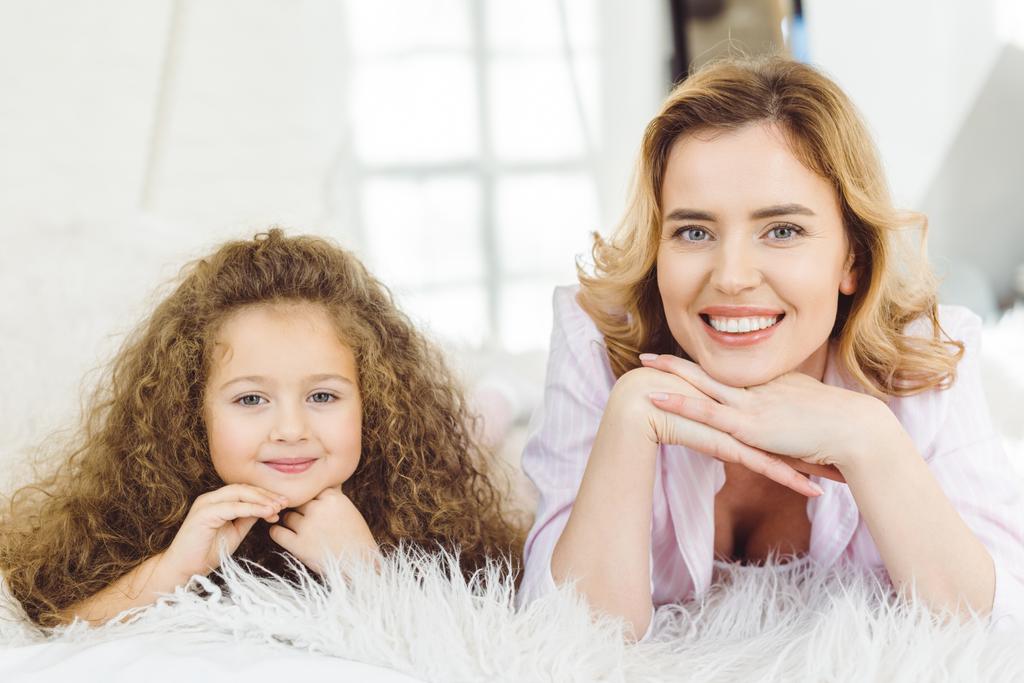 smiling mom and adorable curly daughter lying and looking at camera - Photo, Image