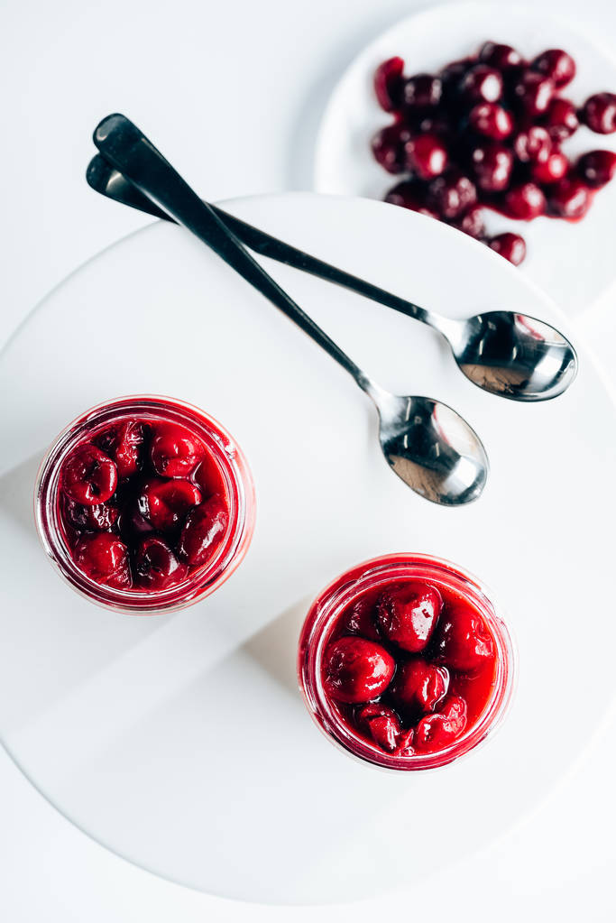 bovenaanzicht van zoete smakelijke cherry dessert in glazen potten op wit - Foto, afbeelding