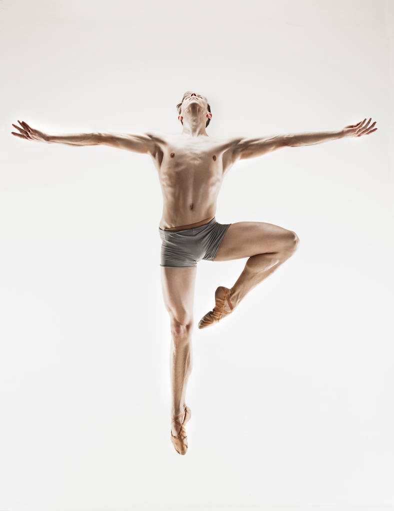 Athletic ballet dancer in a perfect shape performing over the grey background. - Photo, Image