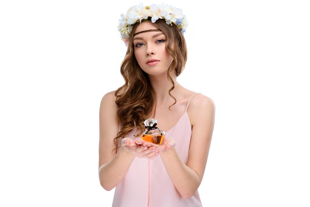 beautiful young woman in floral wreath holding bottle of perfume isolated on white - Photo, Image