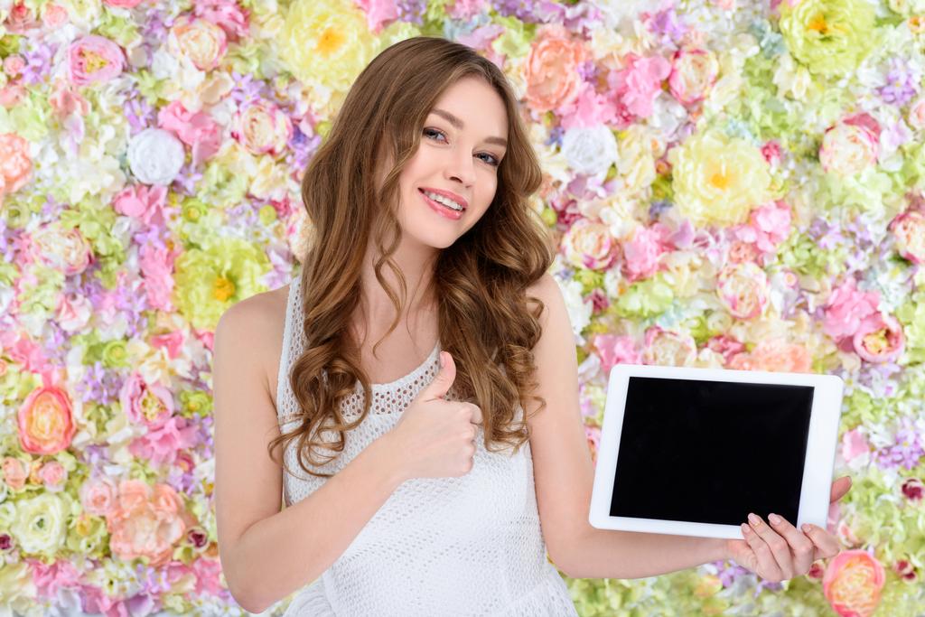 hermosa mujer joven con la tableta que muestra el pulgar hacia arriba en el fondo floral
 - Foto, imagen