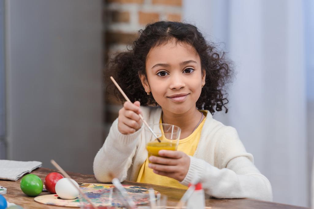 enfant afro-américain mettre pinceau dans le verre avec de la peinture pour peindre des oeufs de Pâques
 - Photo, image