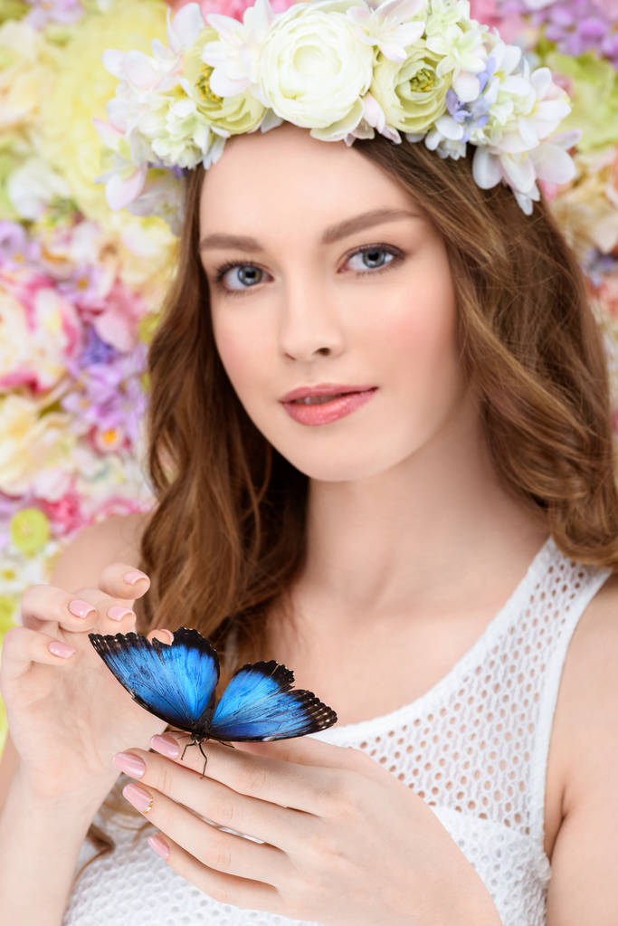 smiling young woman in floral wreath with butterfly on hand - Photo, Image