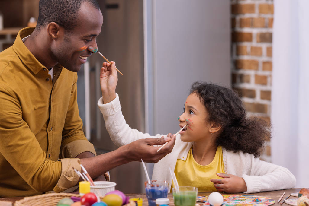 african american father and daughter having fun and painting faces, easter concept - Photo, Image