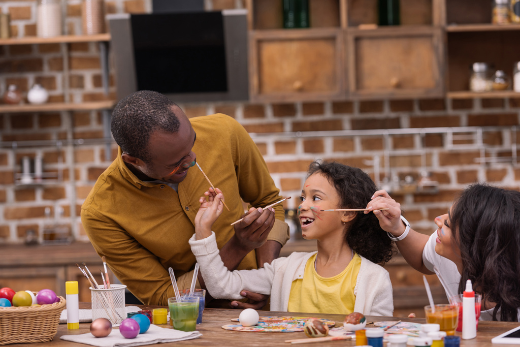 felizes pais e filha afro-americanos se divertindo e pintando rostos
  - Foto, Imagem