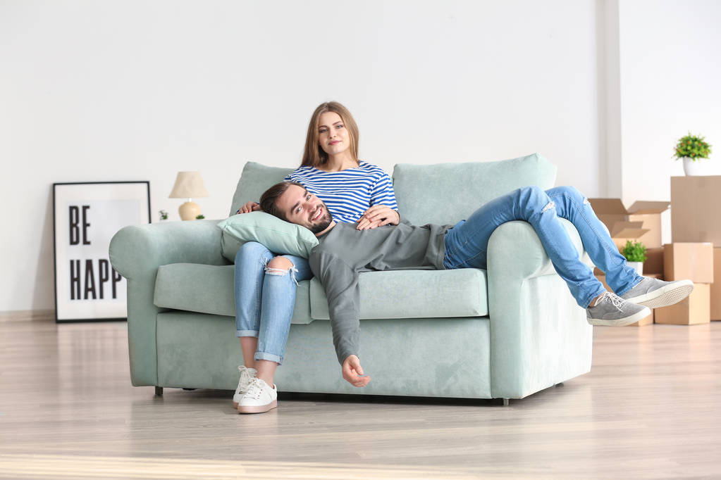 Νεαρό ζευγάρι ακουμπά στον καναπέ μετά τη μετακίνηση σε νέο σπίτι - Φωτογραφία, εικόνα