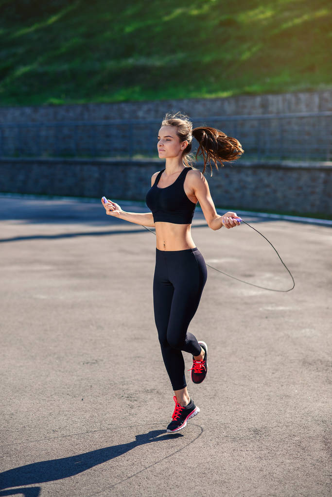 Athlete woman jumping with skipping rope at stadium. Active fitness female doing exercises outdoor. Fitness concept. Healthy lifestyle. - Photo, Image