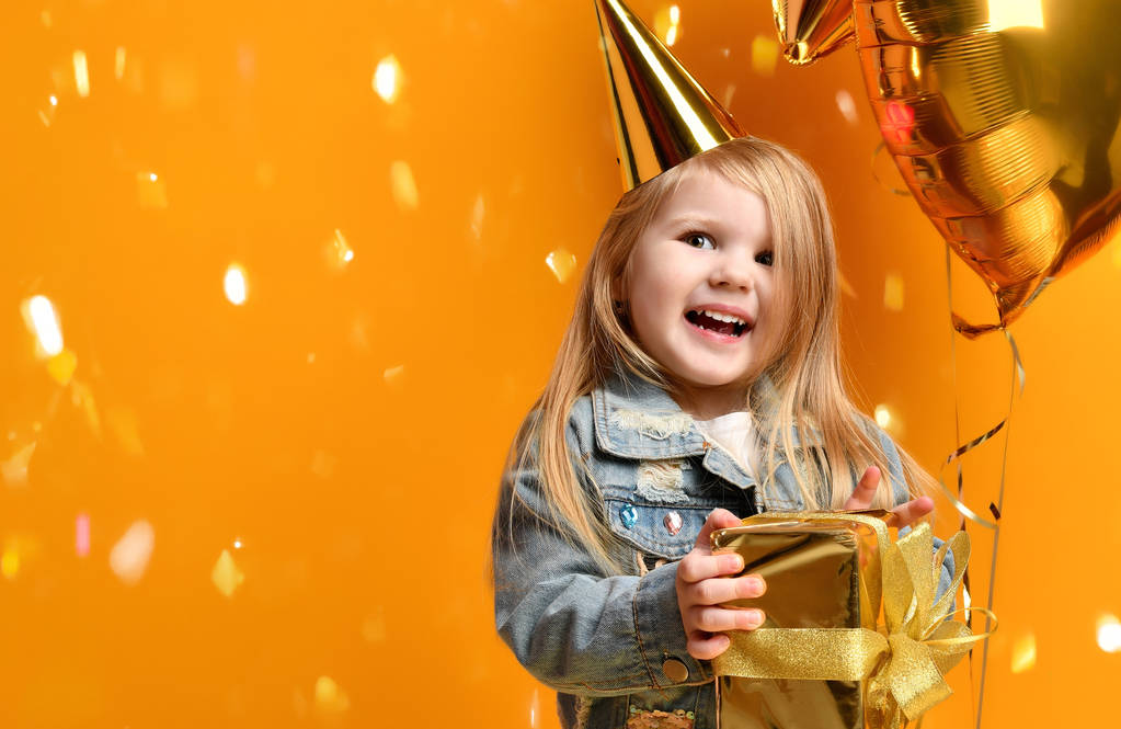 Три роки дівчинка малюк з золотими подарунками повітряні кулі і шапка для дня народження святкування
 - Фото, зображення
