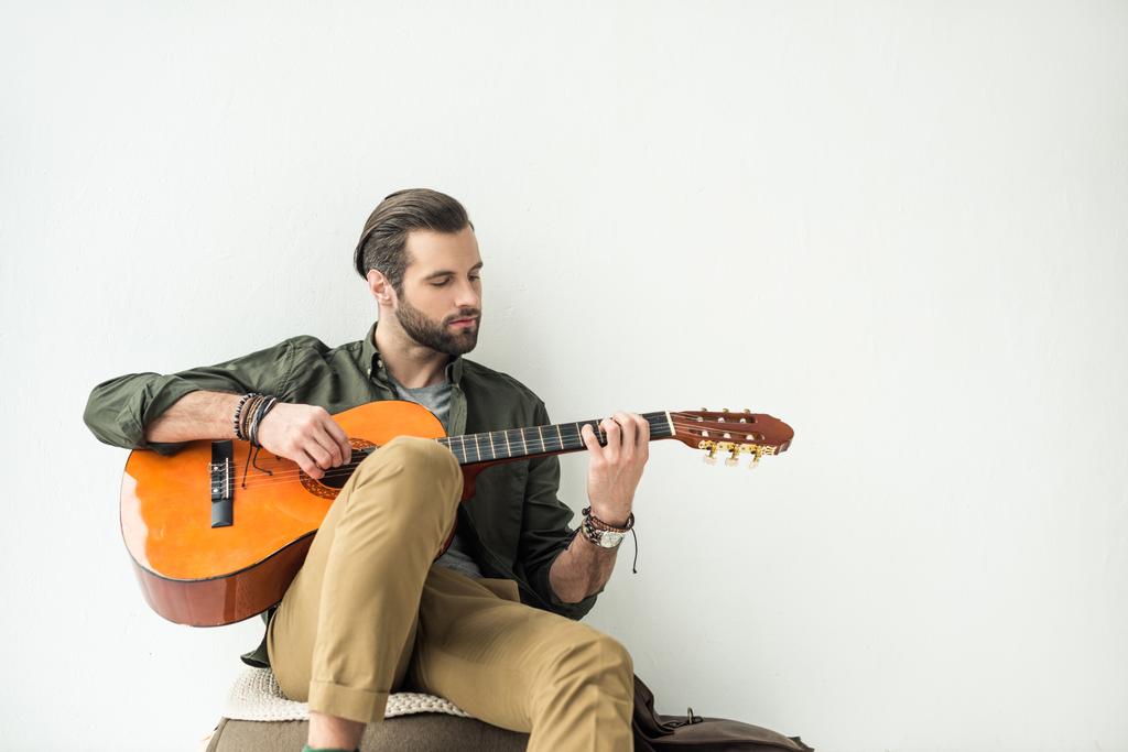 Красивый мужчина играет на акустической гитаре и опирается на стену, изолированную на белом
 - Фото, изображение