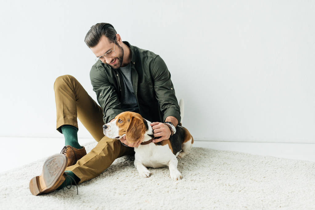 lächelnder schöner Mann spielt mit süßem Beagle auf Teppich - Foto, Bild