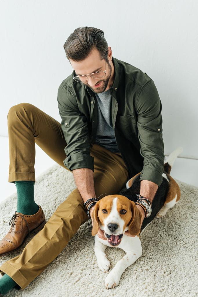 schöner Mann spielt mit gähnend süßem Beagle auf Teppich - Foto, Bild