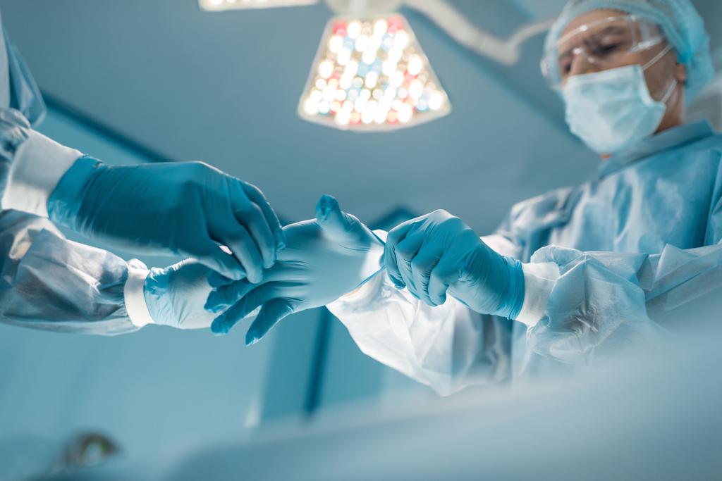 医療用手袋を着用する外科医を支援する看護師のイメージをトリミング - 写真・画像
