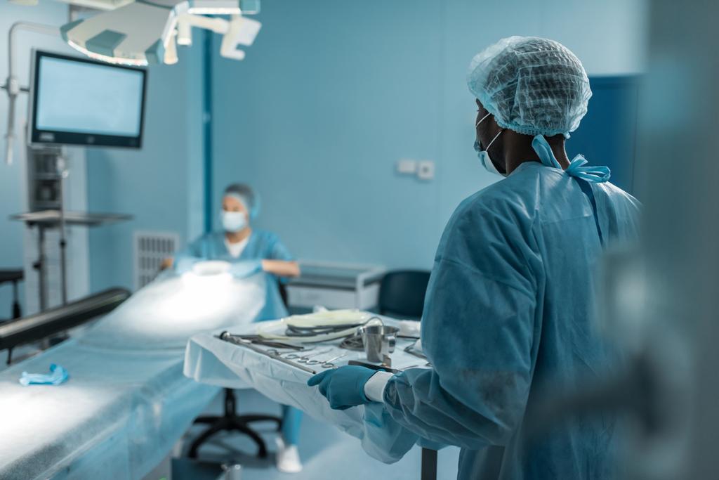 афроамериканський лікар тримає лоток з медичними інструментами для хірургії
 - Фото, зображення