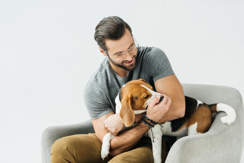 白で隔離の肘掛け椅子に犬と遊んで笑顔のハンサムな男 - 写真・画像