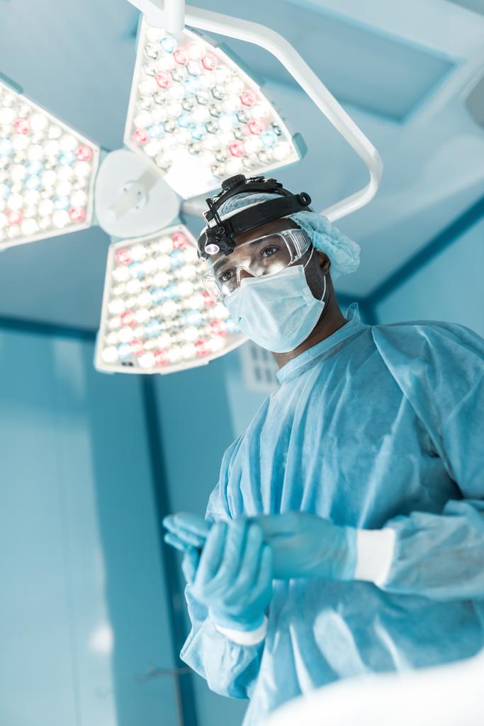 bottom view of african american surgeon wearing medical gloves and looking away - Photo, Image