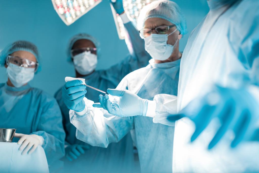 обрезанное изображение врача, передающего медицинский инструмент хирургу
 - Фото, изображение
