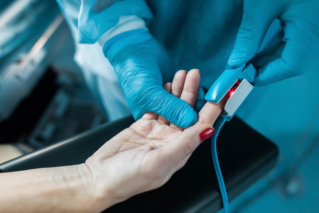 Περικοπή εικόνας του γιατρού φορώντας παλμικό οξύμετρο για ασθενή δάχτυλο στο χειρουργείο - Φωτογραφία, εικόνα
