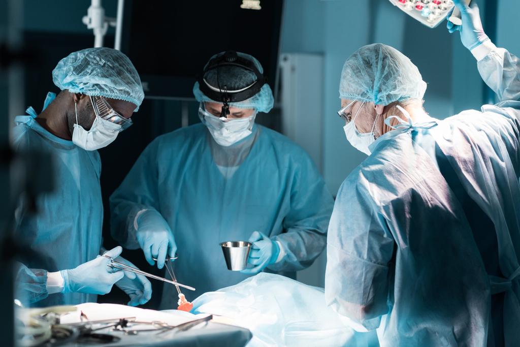 Multiethnische Chirurgen in medizinischen Masken operieren Patienten im Operationssaal - Foto, Bild