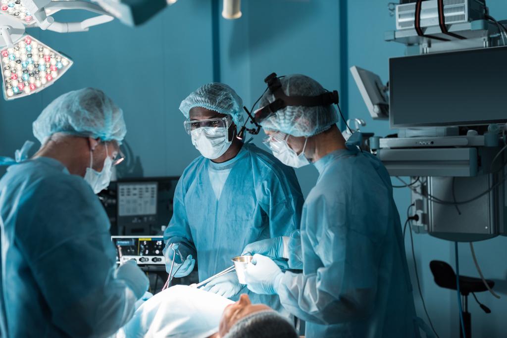 Cirurgiões multiculturais operando paciente em centro cirúrgico
 - Foto, Imagem