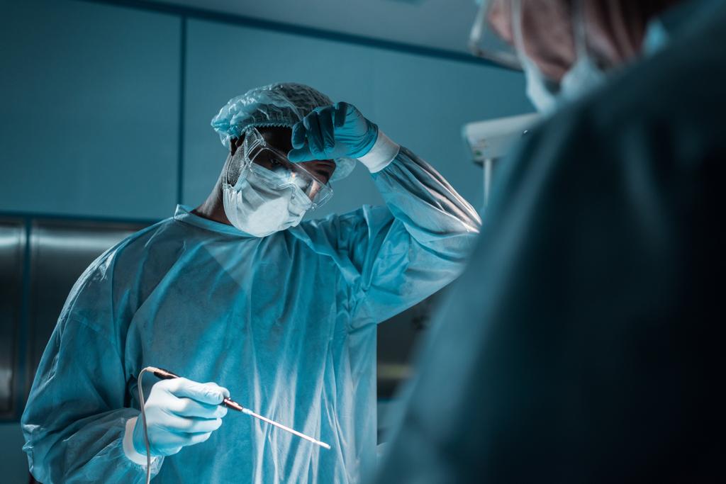 chirurgo afroamericano che tocca la fronte durante l'intervento chirurgico
 - Foto, immagini