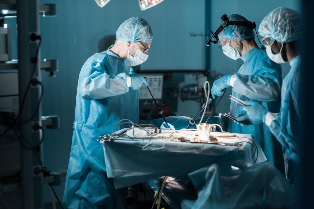side view of multiethnic surgeons operating patient in operating room - Photo, Image