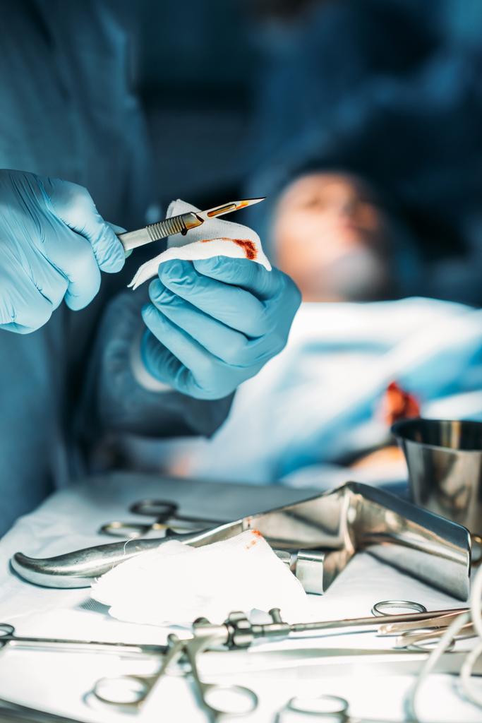 cropped image of surgeon cleaning scalpel from blood in surgery room - Photo, Image