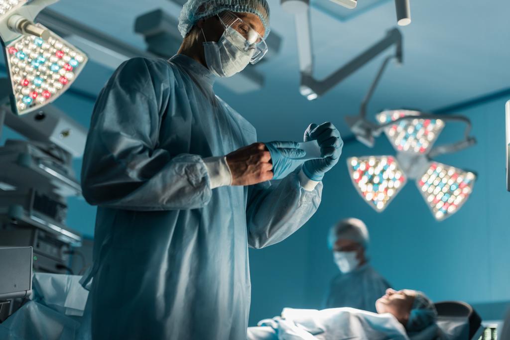 Chirurg zieht medizinische Handschuhe in der Nähe des Patienten im Operationssaal aus - Foto, Bild