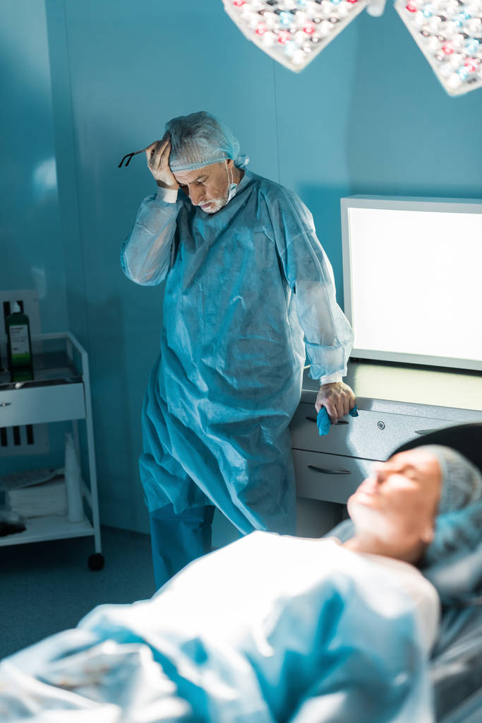 uitgeput arts permanent in de buurt van patiënt in operatie kamer - Foto, afbeelding