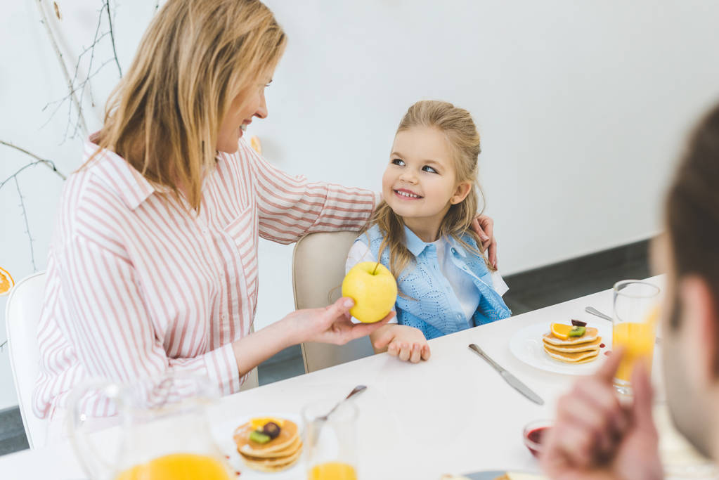 madre che dà mela a figlia durante la colazione a casa
 - Foto, immagini