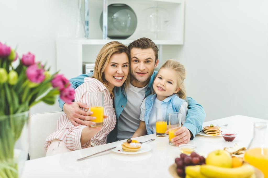 πορτρέτο του χαμογελώντας γονείς και κόρη που βλέπουν τα φωτογραφικών μηχανών κατά τη διάρκεια του πρωινού στο σπίτι - Φωτογραφία, εικόνα