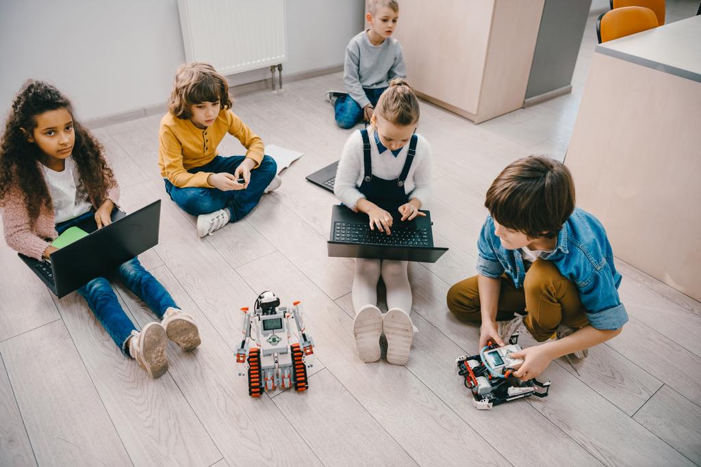 высокий угол зрения детей программирования робота, сидя на полу в классе стволового образования
 - Фото, изображение
