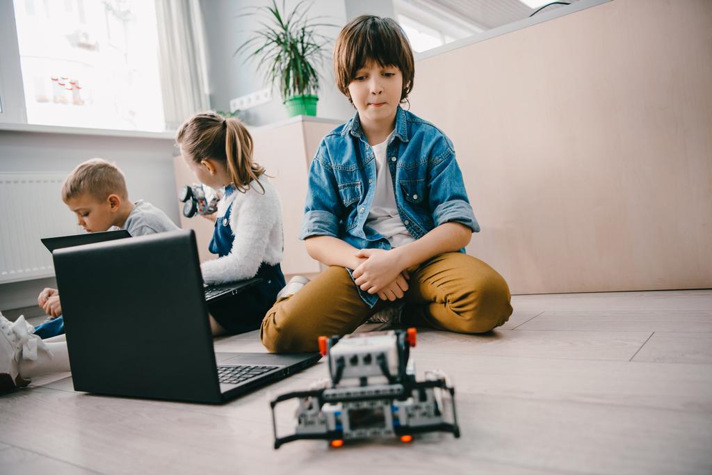 adolescent écolier avec ordinateur portable et robot assis sur le sol à la classe de machines
 - Photo, image