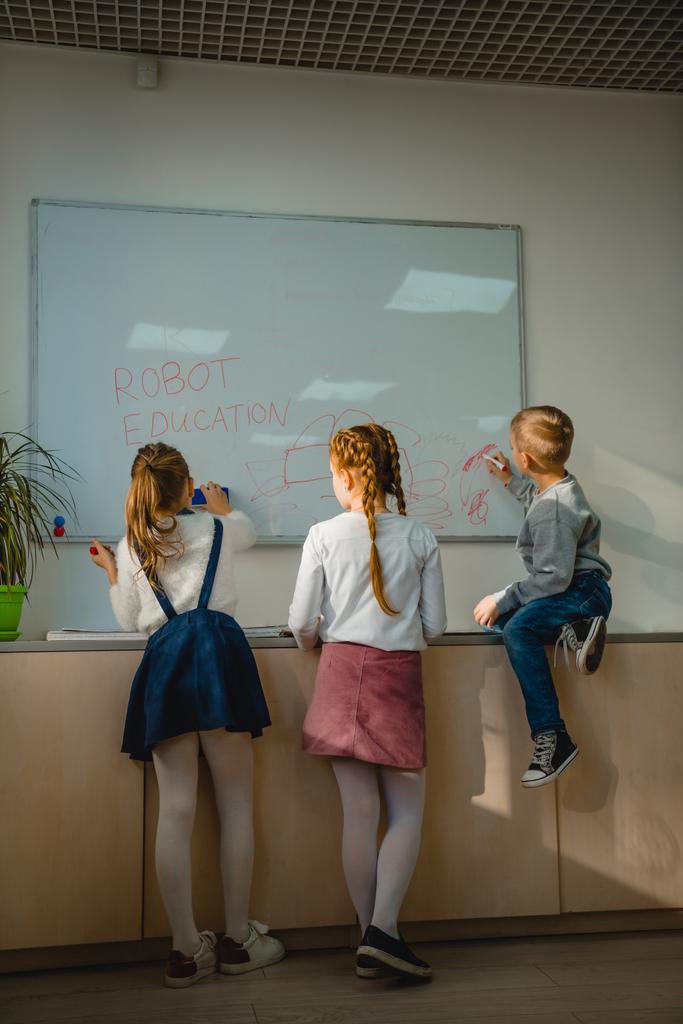 vista posterior de los niños escribiendo y dibujando señales de educación robot en pizarra blanca
 - Foto, Imagen