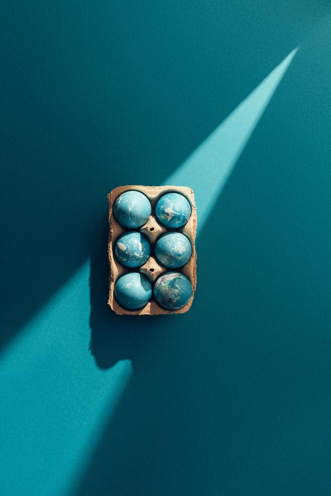vista dall'alto di uova di Pasqua blu in vassoio, su blu con raggio di sole
 - Foto, immagini
