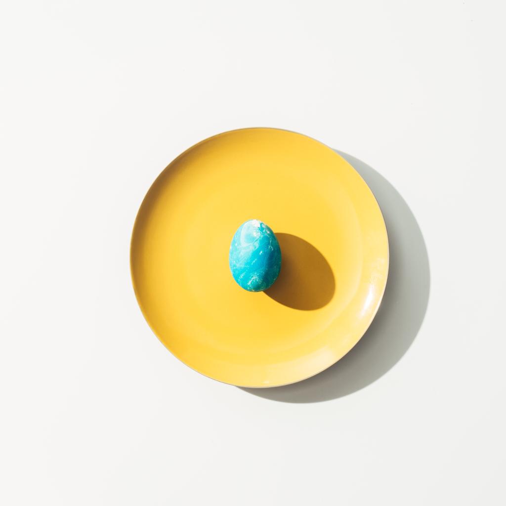 vista superior del huevo de Pascua azul en la placa amarilla, en blanco
 - Foto, Imagen