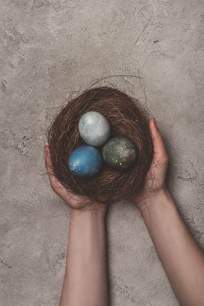 oříznutý pohled člověka drží hnízdo s velikonoční vajíčka na betonový podklad  - Fotografie, Obrázek