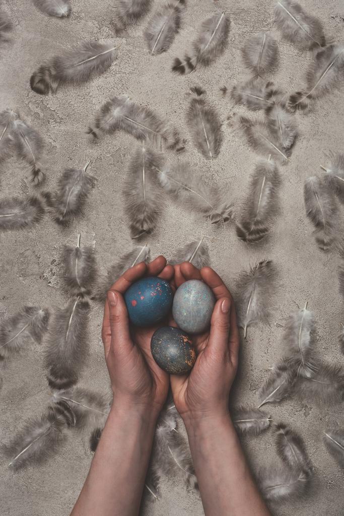 cropped view of man holding easter eggs on concrete surface with feathers - Photo, Image