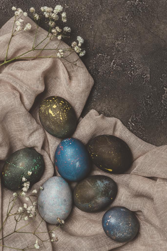 верхний вид потрепанных окрашенных пасхальных яиц и цветов на скатерти
  - Фото, изображение