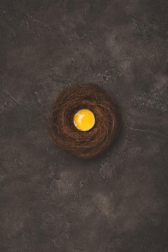 верхний вид разбитого яйца с желтком в гнезде на бетонной поверхности
  - Фото, изображение