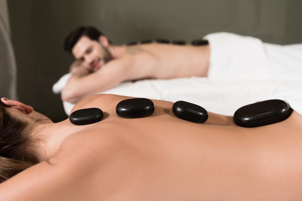 abgeschnittene Aufnahme eines Paares, das sich bei einer Massage mit heißen Steinen im Wellness-Center ansieht  - Foto, Bild