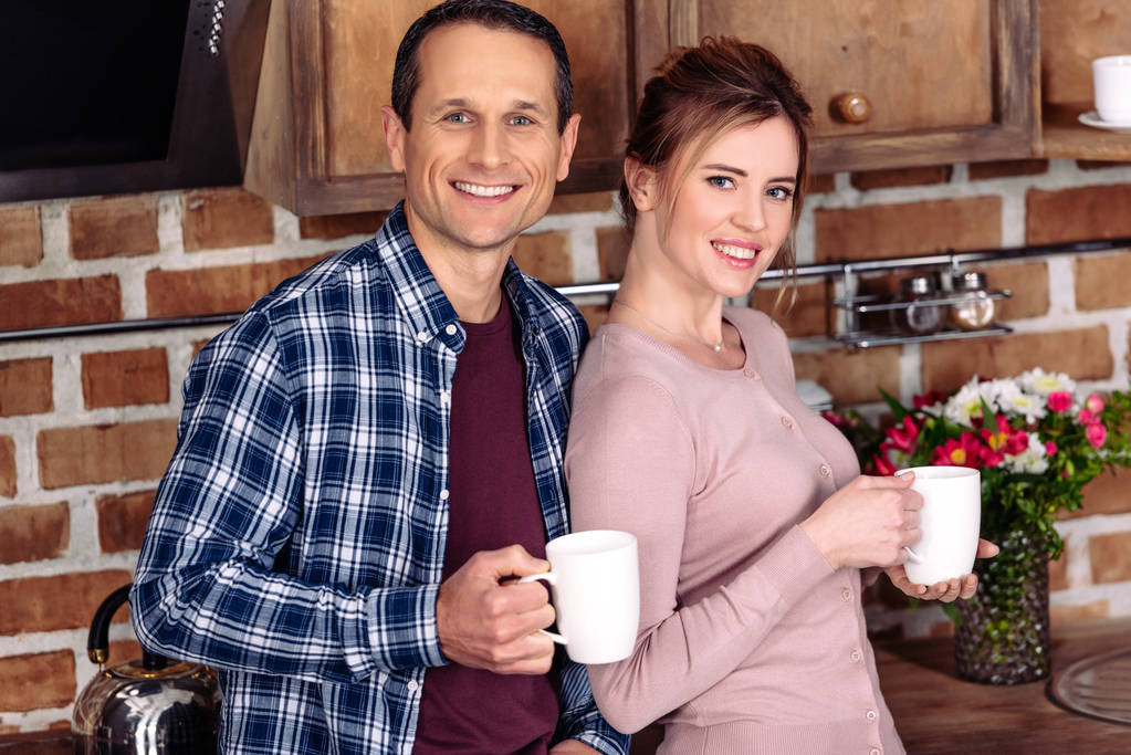 Porträt von lächelnder Frau und Mann mit Tassen Kaffee in der heimischen Küche - Foto, Bild