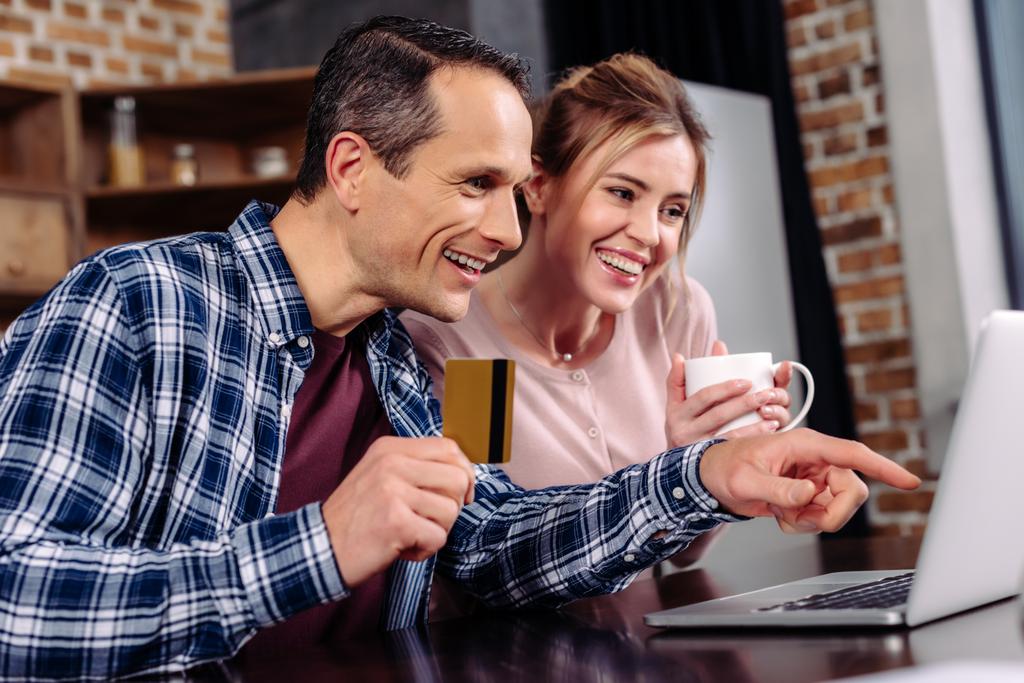 szczęśliwa para z karty kredytowej i filiżankę kawy, patrząc na ekran laptopa w domu - Zdjęcie, obraz