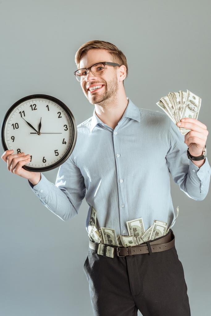 Para ve gri izole saati gösteren genç gülümseyen iş adamı - Fotoğraf, Görsel