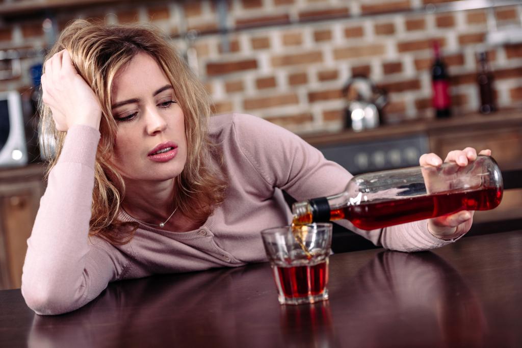 donna versando alcol nel bicchiere mentre seduto a tavola in cucina
 - Foto, immagini