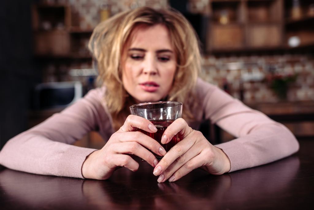 portrait of drunk woman with glass of alcohol sitting t table at home - Photo, Image