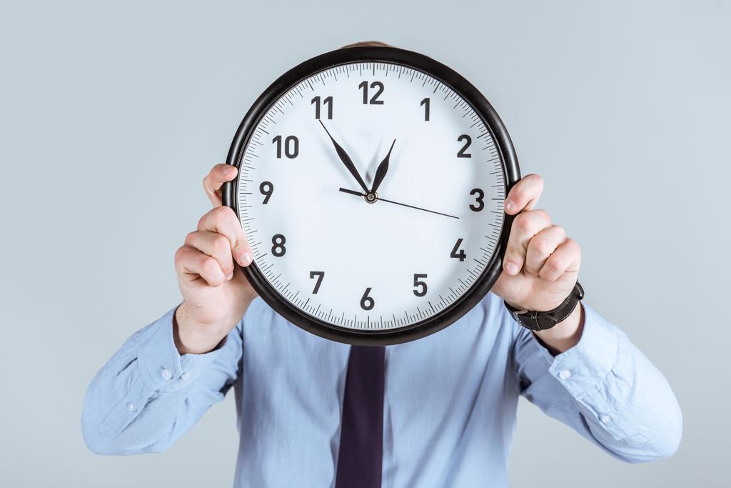 Businessman in shirt holding clock over his face isolated on grey  - Photo, Image