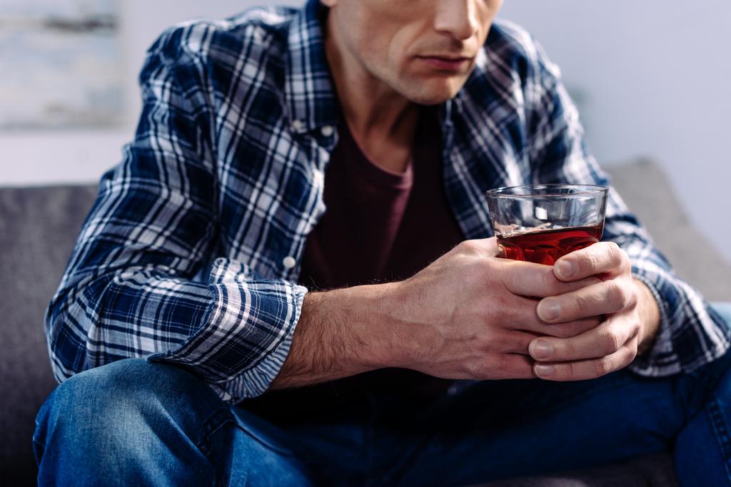 částečný pohled člověka s pitím alkoholu sedí na gauči doma - Fotografie, Obrázek