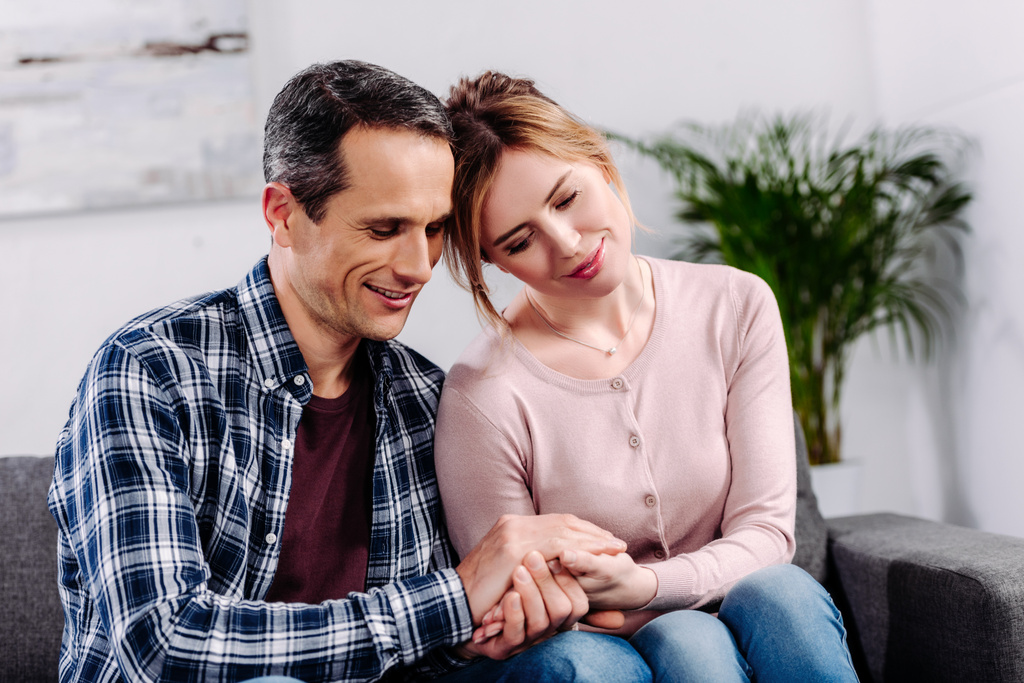 vrouw en man hand in hand tijdens het rusten op de sofa thuis - Foto, afbeelding